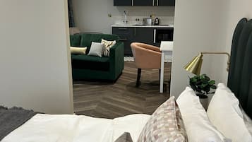 A modern bedroom with a large bed, a green sofa, and a kitchen in the background.