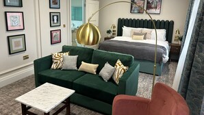 A hotel room with a green sofa, a red chair, a bed with a dark headboard, and artwork on the walls. - TheHillbrookSherborne (Sherborne)