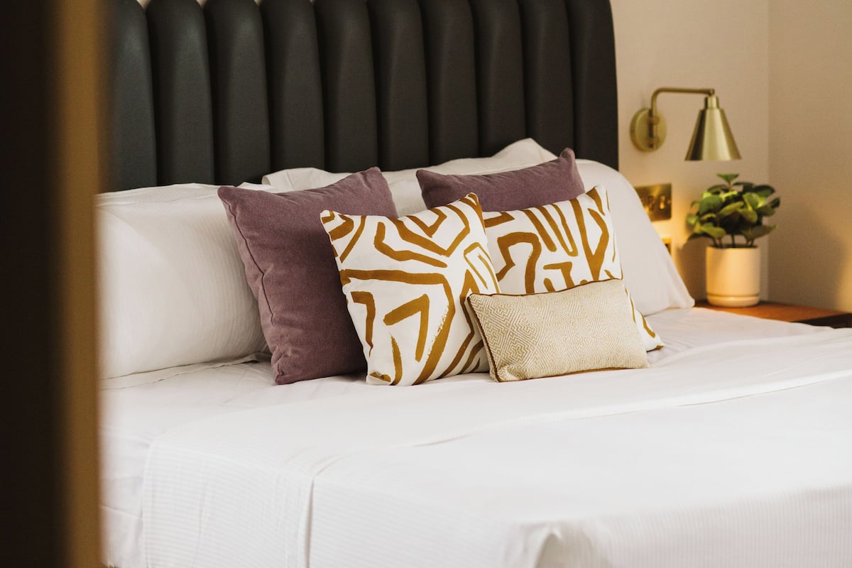 A neatly made bed with white and patterned pillows, a black headboard, and two abstract paintings on the wall.
