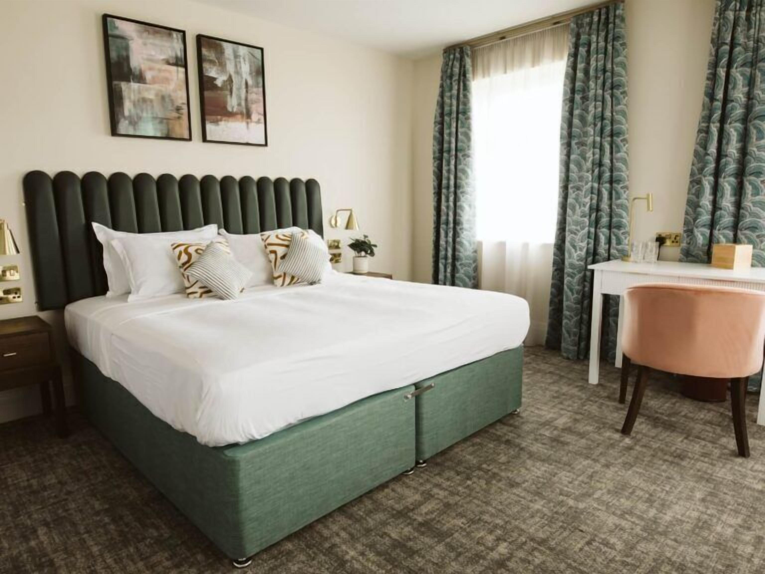 A hotel room with a bed, a desk, a chair, and curtains.