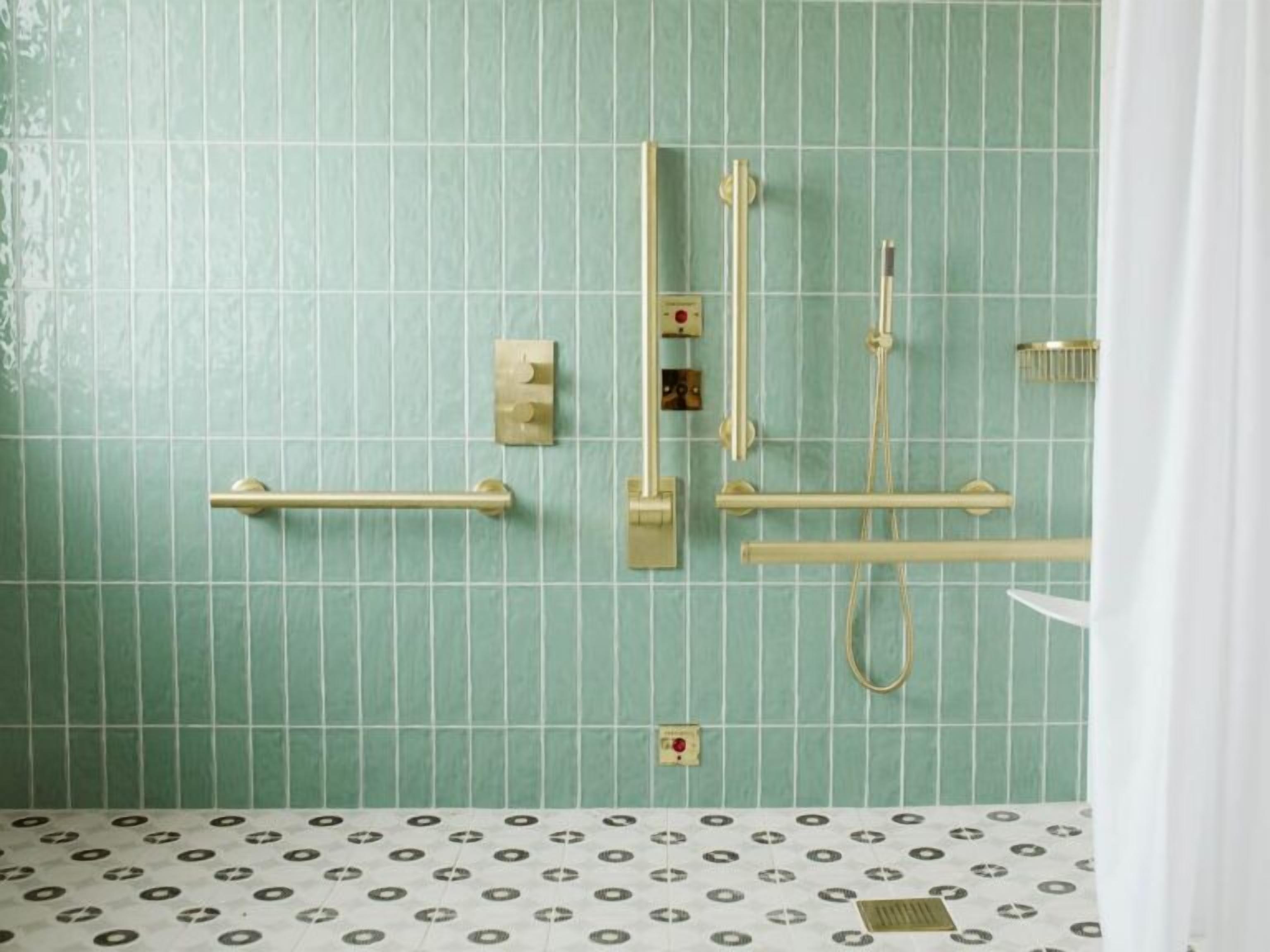 Ein Badezimmer mit grüner Fliesenwand, weißem Fußboden mit Muster und einer goldfarbenen Duschsteuerung.
