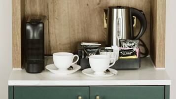 Una kitchenette con cafetera, dos tazas blancas, un infusor de té y cápsulas de café.