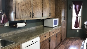 Een keuken met houten kastjes, een magnetron, een vaatwasser en een raam met gordijnen.