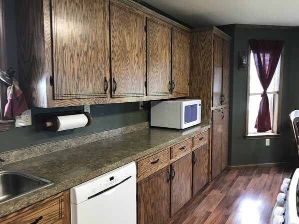 A kitchen with wooden cabinets, a microwave, a dishwasher, and a window with curtains.