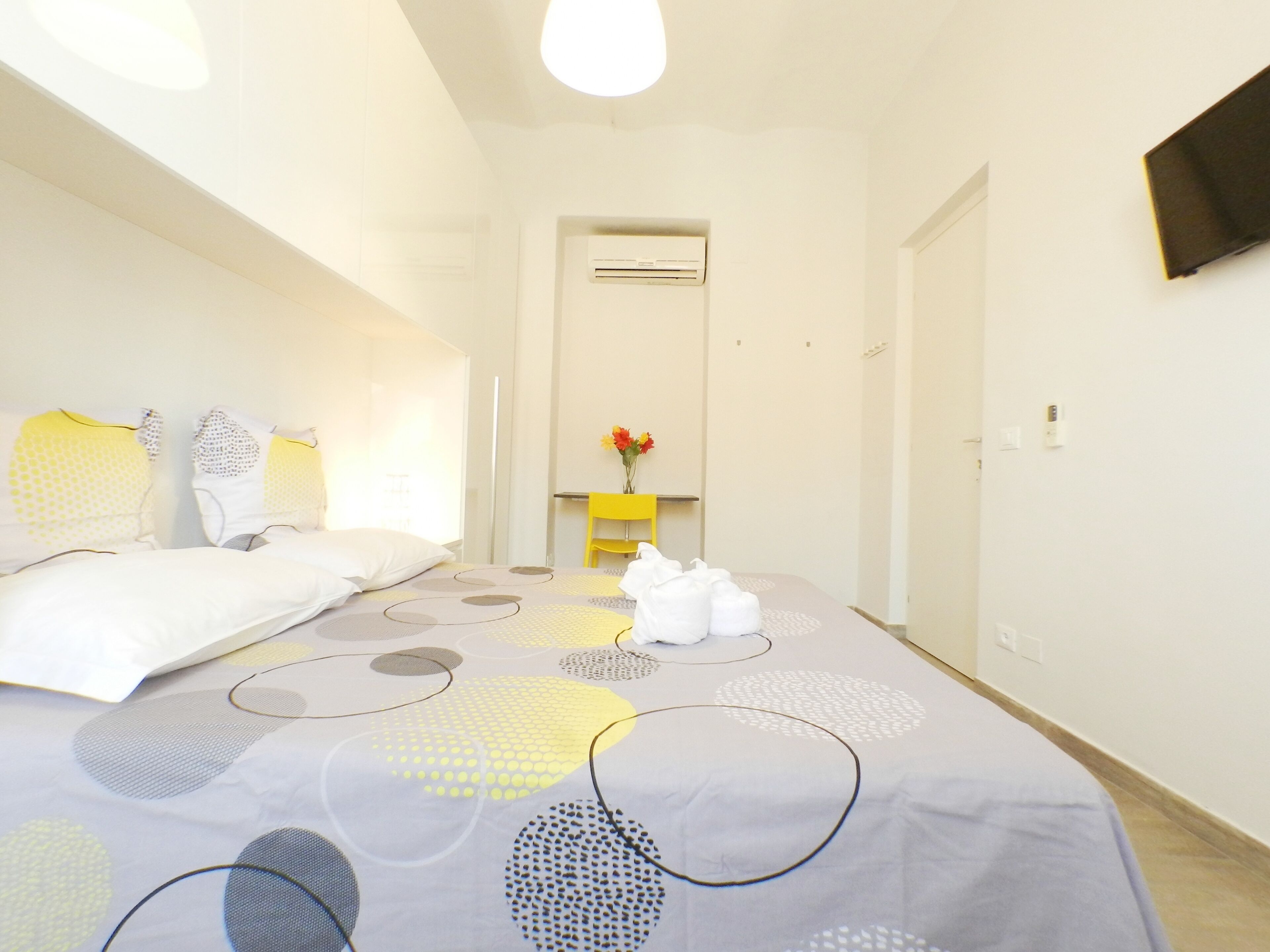 Habitación de hotel con una cama, un escritorio y una silla. Hay un televisor montado en la pared y un equipo de aire acondicionado.