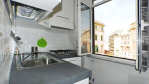 Eine Küche mit Gaskochfeld, Spüle aus Edelstahl und Fenster mit Blick auf Gebäude.