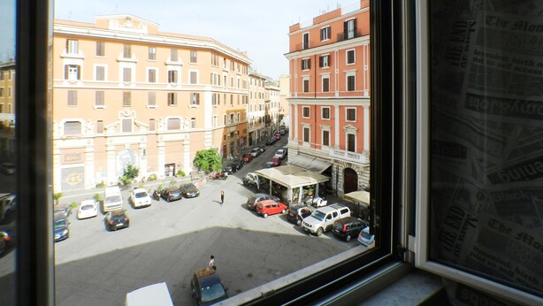 Blick aus einem Fenster auf eine Straße mit Gebäuden, parkenden Autos und blauem Himmel.