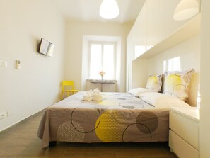 Une chambre d’hôtel avec un lit, une chaise, une petite table avec un vase et un téléviseur fixé au mur.