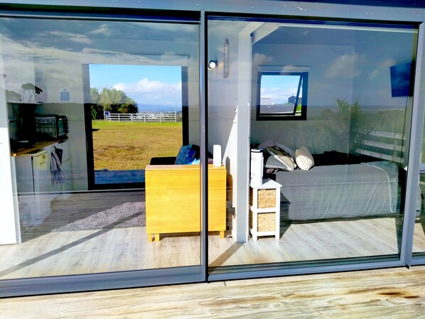 A modern interior with a bed, a small wooden dresser, a television, and a window with a view of a grassy field.