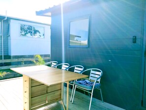 A wooden deck with a table and chairs, a small window, and a door. - Seascape Peninsula Bach (Karikari Peninsula)