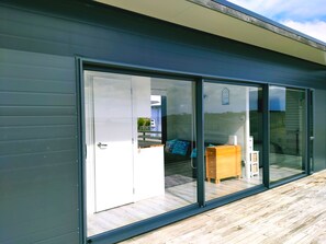 A modern building with a sliding glass door leading to an outdoor area with a wooden deck. - Seascape Peninsula Bach (Karikari Peninsula)