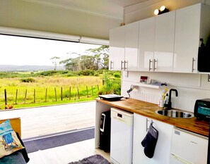 A modern kitchen with white cabinets, a wooden countertop, and a view of a grassy landscape. - Seascape Peninsula Bach (Karikari Peninsula)