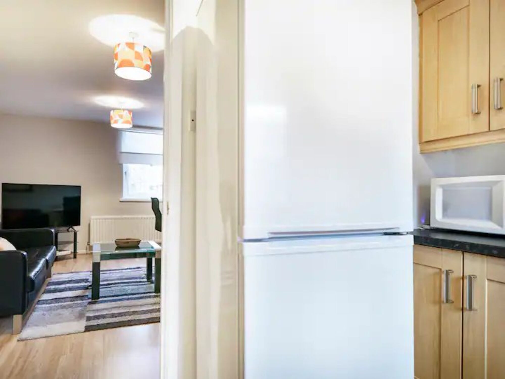 A modern kitchen with a white refrigerator, wooden cabinets, and a microwave.