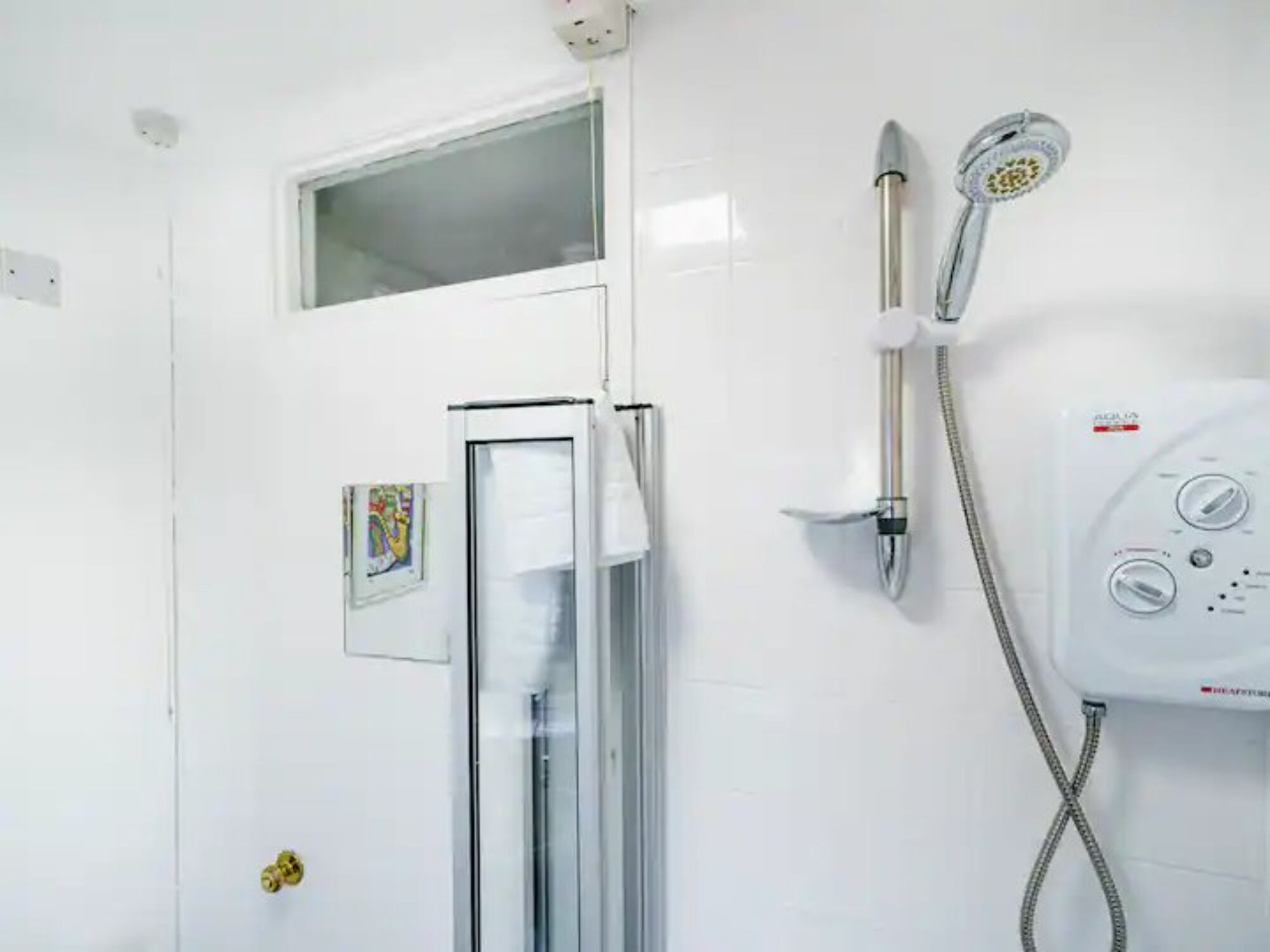 A bathroom with a glass shower enclosure, a handheld showerhead, and a wall-mounted control panel.