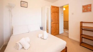 A bedroom with a bed, a wooden door, a small table, and a shelf.