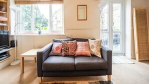 A living room with a dark brown sofa, a small table, a bookshelf, and a window with blinds.