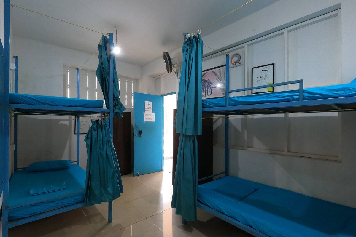 A dormitory room with bunk beds, a door with a sign, and a ceiling fan.