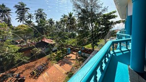 Blick vom Balkon auf einen Garten mit Palmen, einem Feldweg und einem blauen Geländer.