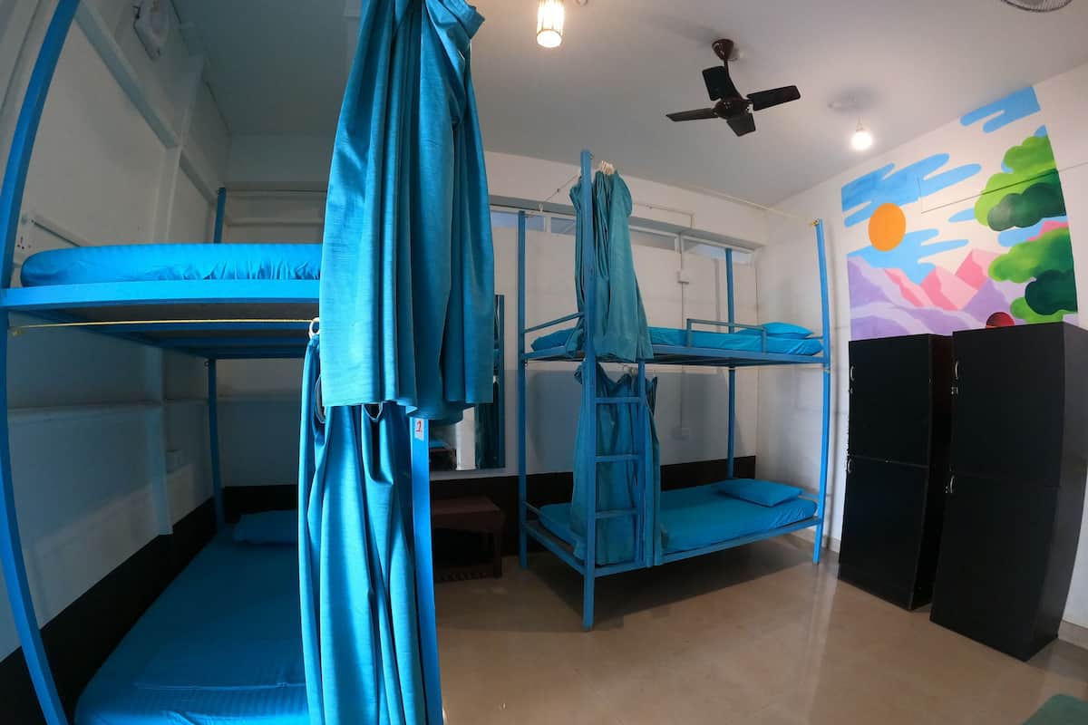 A dormitory room with bunk beds, a ceiling fan, and a colorful mural on the wall.