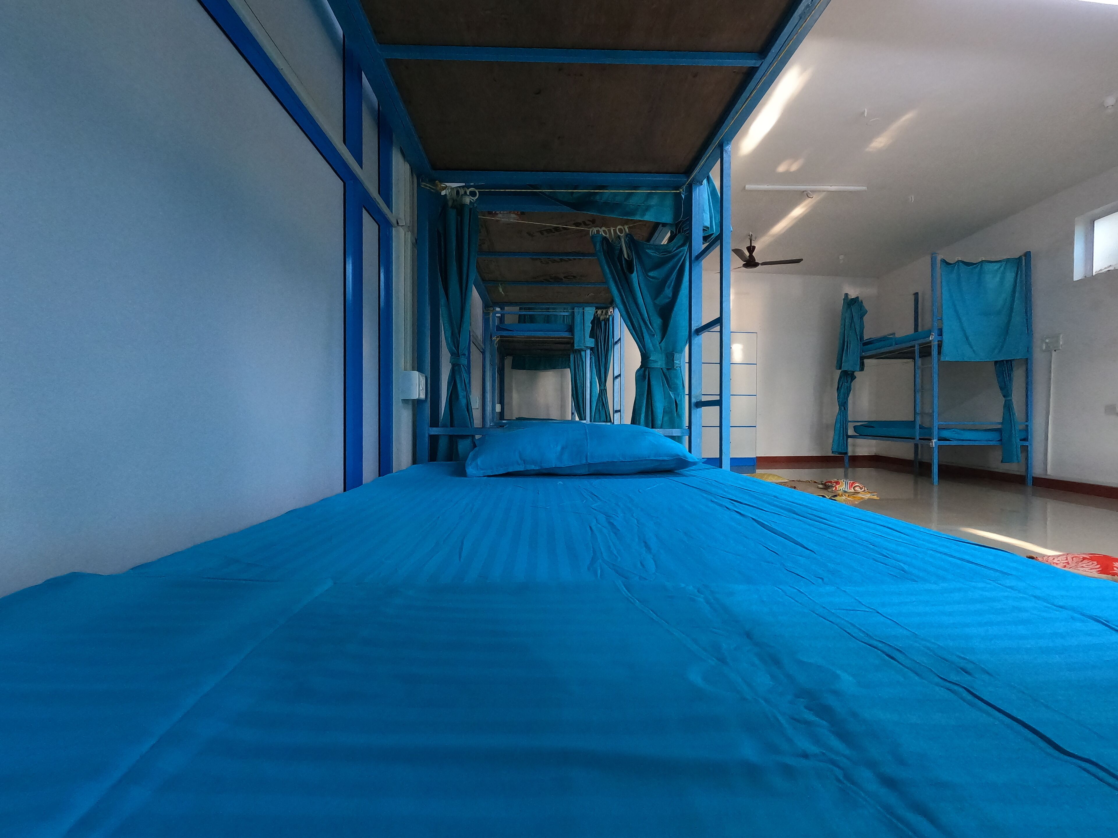 Une chambre de dortoir avec des lits superposés, un ventilateur de plafond et des rideaux.