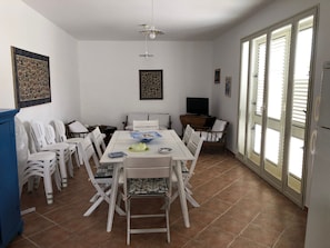 Uma sala de jantar com uma mesa, cadeiras, uma televisão e uma janela com persianas.