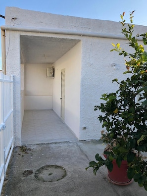 Entrada de edifício com fachada de concreto, portão de metal e planta em vaso.