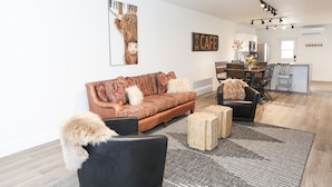 A modern living room with a sofa, a coffee table, and a dining area with chairs and a table. - Newly-remodeled cozy condo, downtown Manhattan, MT! (Manhattan)