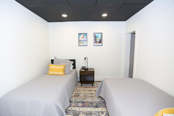 A bedroom with two beds, a nightstand, a lamp, and two framed pictures on the wall.