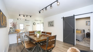 A spacious dining area with a wooden table and chairs, a kitchen in the background, and a sliding door leading to a bedroom. - Newly-remodeled cozy condo, downtown Manhattan, MT! (Manhattan)