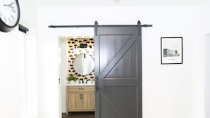 A room with a sliding barn door, a round mirror, a framed picture on the wall, and a clock on the wall. - Newly-remodeled cozy condo, downtown Manhattan, MT! (Manhattan)