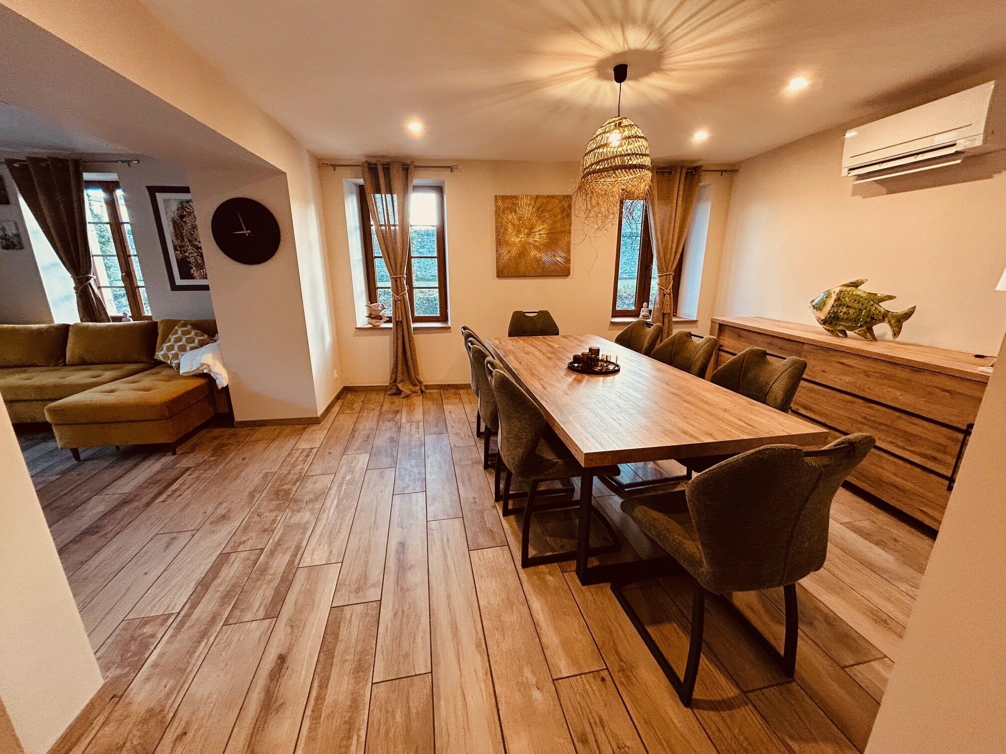 A modern living space with a wooden dining table, a sofa, and a kitchen area.