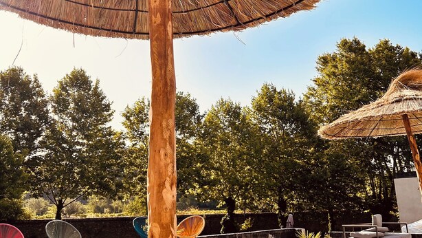 A pool area with a thatched umbrella, lounge chairs, and a pool.