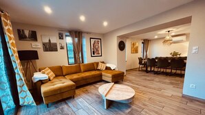 A modern living room with a sectional sofa, a round coffee table, and a dining area with a chandelier.