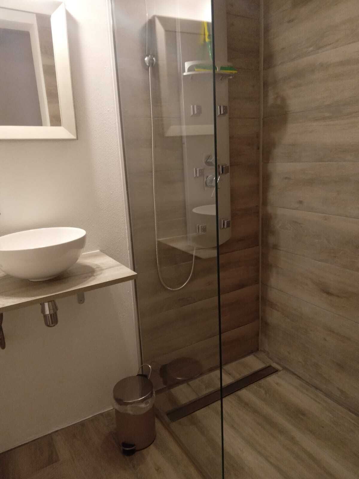 A modern bathroom with a glass-enclosed shower, a white sink, and a wooden floor.