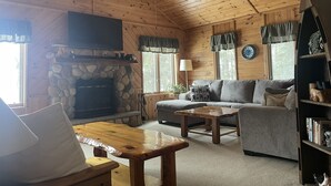 A cozy cabin interior with a stone fireplace, wooden ceiling, and a sofa set.