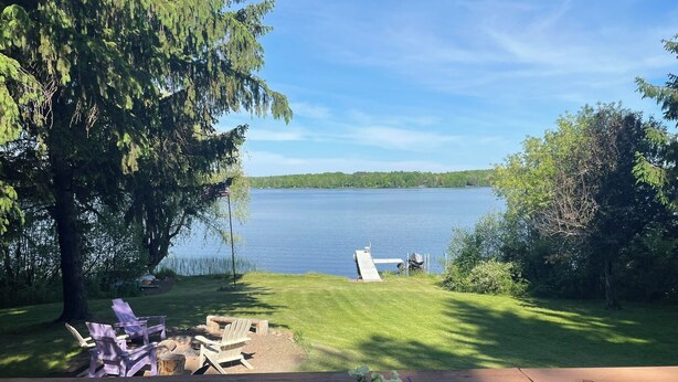 A lakeside deck with a checkered table, chairs, and a flower arrangement.