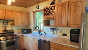 A kitchen with wooden cabinets, stainless steel appliances, a clock, and a window with a view of trees.