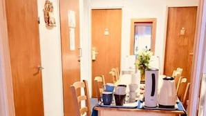 A hotel dining area with a wooden table, chairs, a coffee pot, and a vase of flowers.