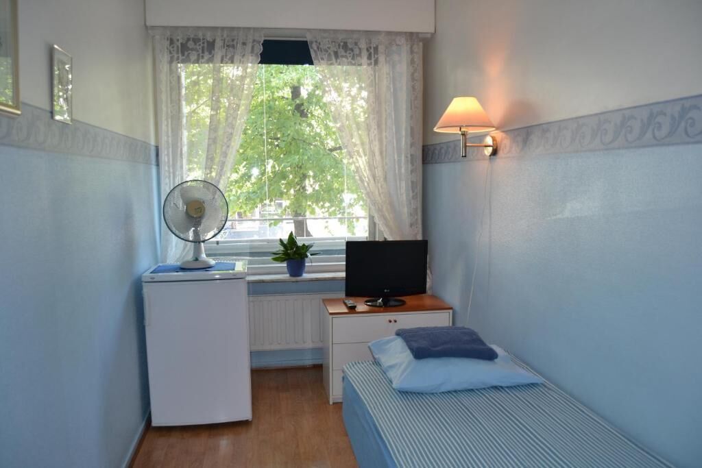 Un dormitorio con cama, un escritorio con computadora, una lámpara y una ventana con cortinas.