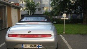 A silver convertible car parked on a street with a building in the background.