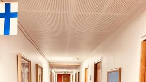 A hotel corridor with framed pictures on the walls, a reception desk, and doors leading to rooms.