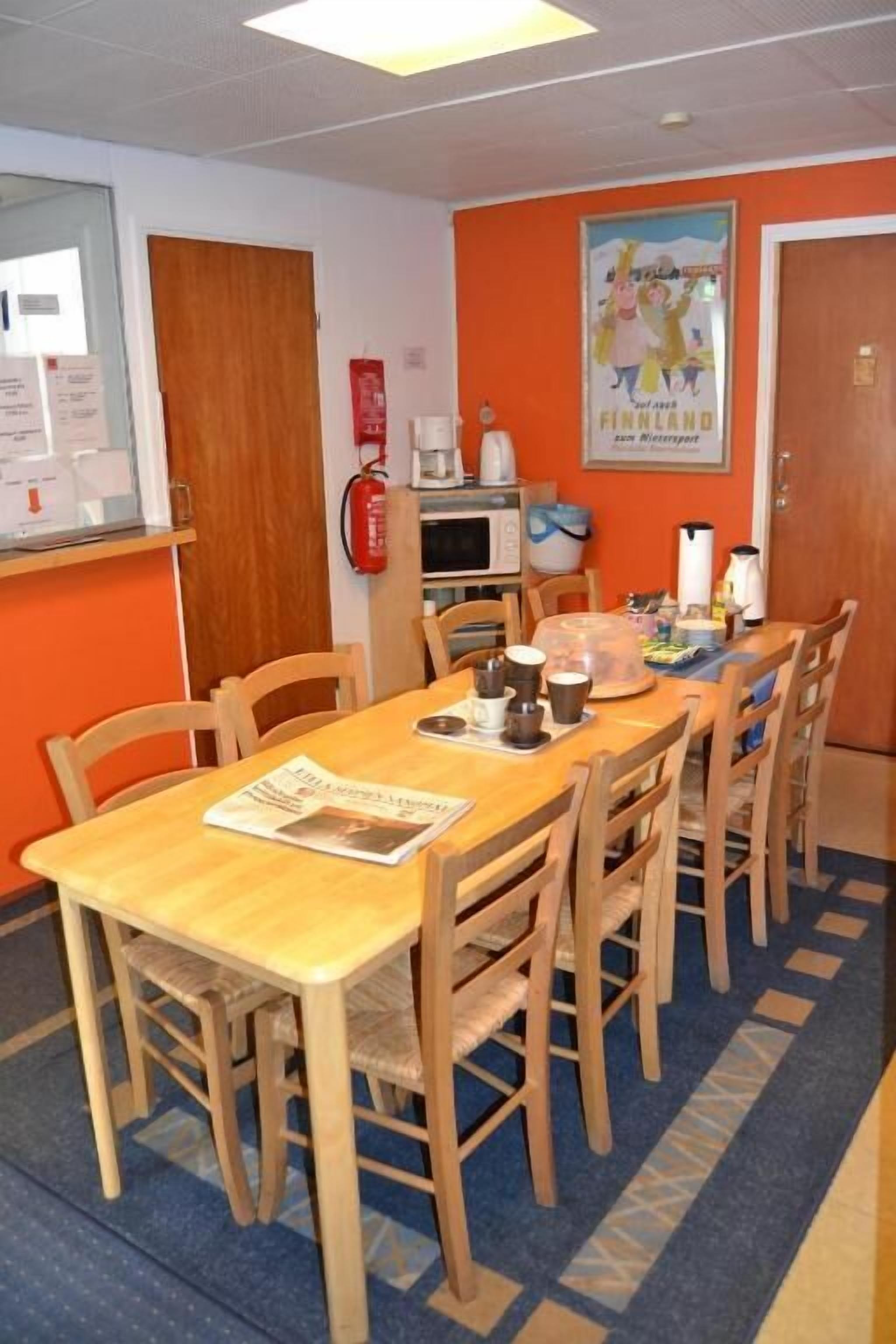 A dining area with a long wooden table and chairs, a fire extinguisher, a microwave, and a poster on the wall.