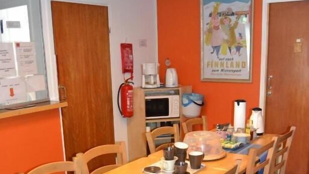 A dining area with a long wooden table and chairs, a fire extinguisher, a microwave, and a poster on the wall.