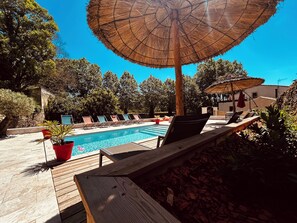 A poolside area with lounge chairs, a wooden deck, and a thatched umbrella.