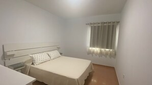 Quarto pequeno e limpo com uma cama de solteiro, mesa de cabeceira e janela com cortinas.