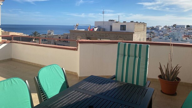 Terraço no telhado com mesa e cadeiras, com vista para a paisagem costeira e o mar.