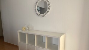 Um console branco com gavetas e uma prateleira, um espelho redondo com moldura treliçada e uma pequena bicicleta decorativa na prateleira.