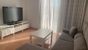 Uma sala de estar moderna com uma TV de tela plana em um móvel branco, um sofá cinza e uma mesa de centro branca.