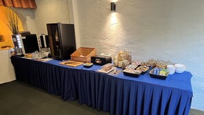 A buffet table with various food items and condiments, a black refrigerator, and a wall-mounted light fixture. - Hotel Elsen (Grevenbroich)