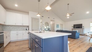 A spacious kitchen with white cabinets, a blue island, and a large window.